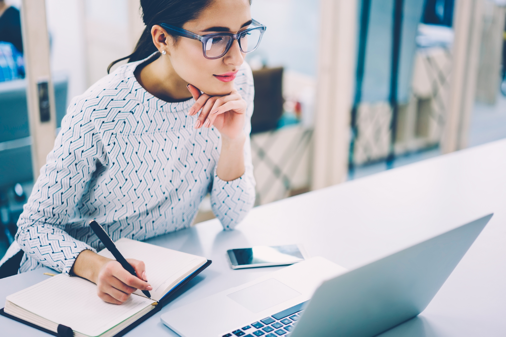 Woman reading publications on laptop and taking notes